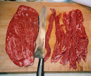 Beef being cut into jerky sized slices. 