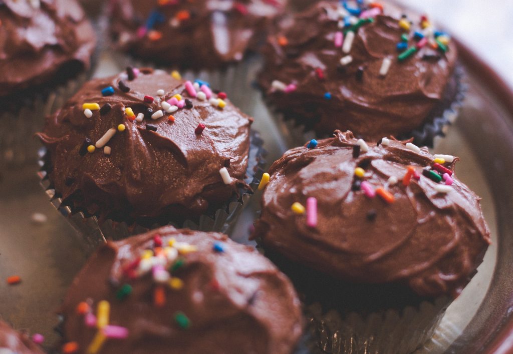 Plate with chocolate frosted cupcakes with sprinkles.