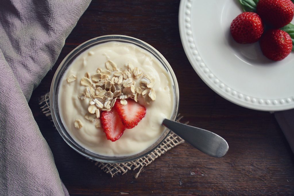 Plain yogurt topped with raw oatmeal and cut berries. A side dish with whole berries is nearby.