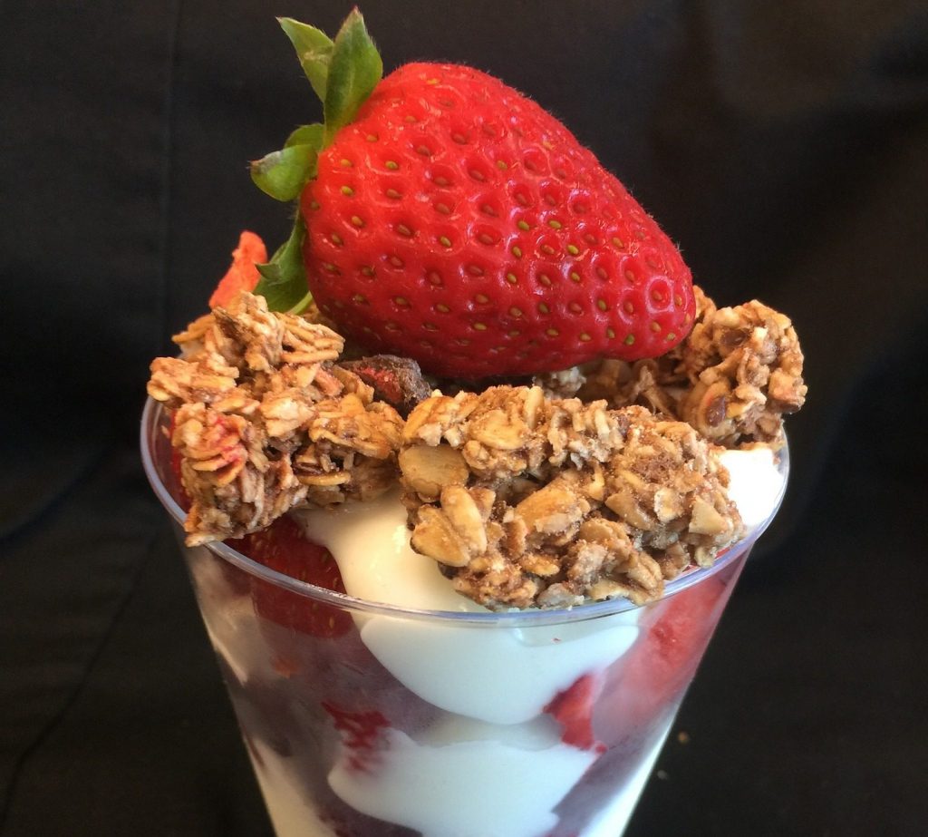 Small yogurt parfait, layered with yogurt, fresh berries, and topped with granola and one whole strawberry.