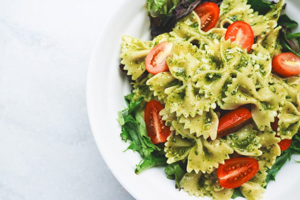 Cooked bow-tie pasta with pesto and tomatoes on top of salad greens.
