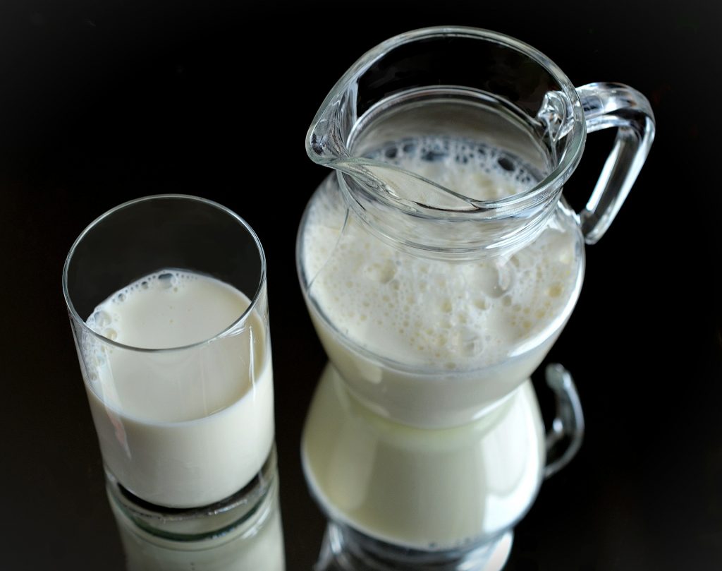 Milk in pitcher next to small glass of milk.