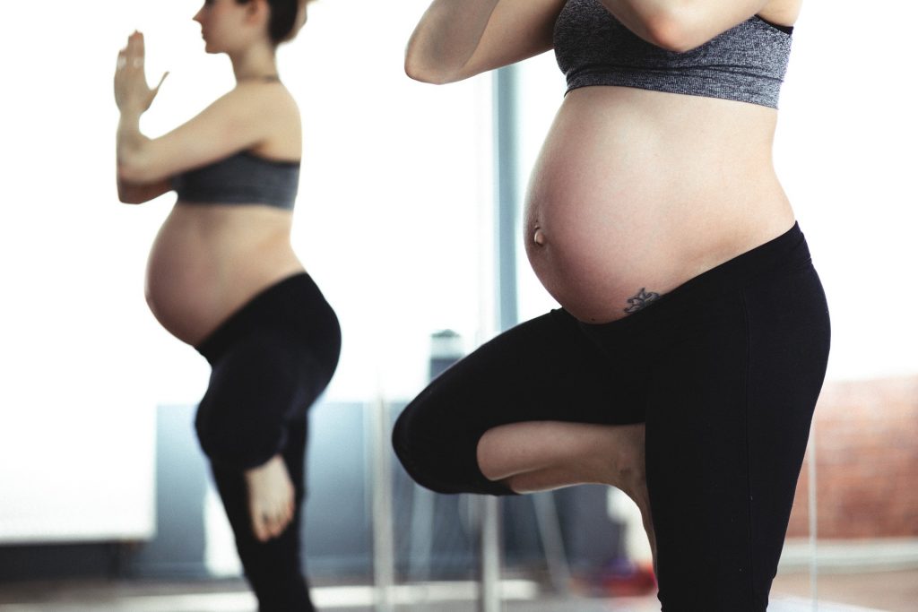 Pregnant woman doing yoga with belly showing.