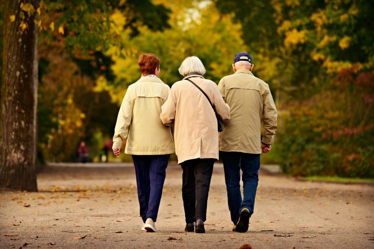 Three older adults walking together on a paved path during the fall.