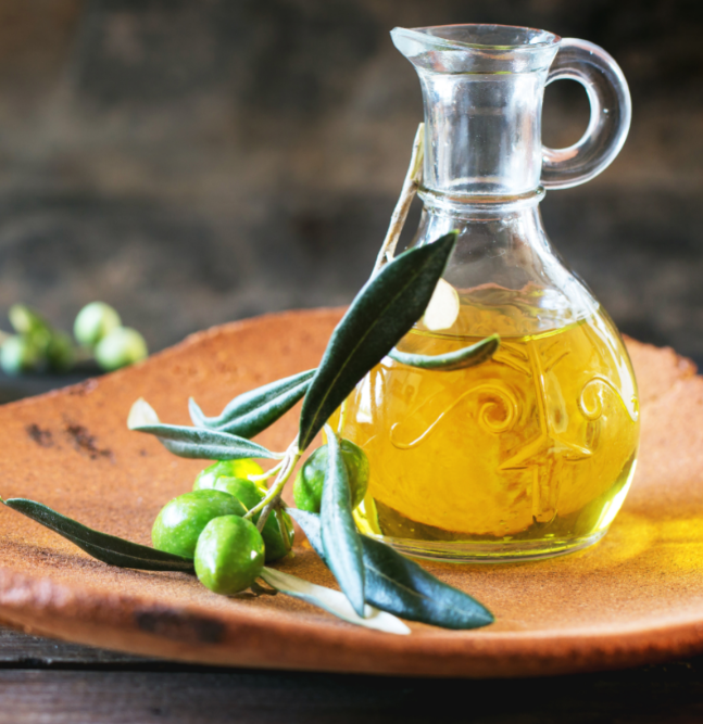 Olive oil in glass jar beside whole olives.