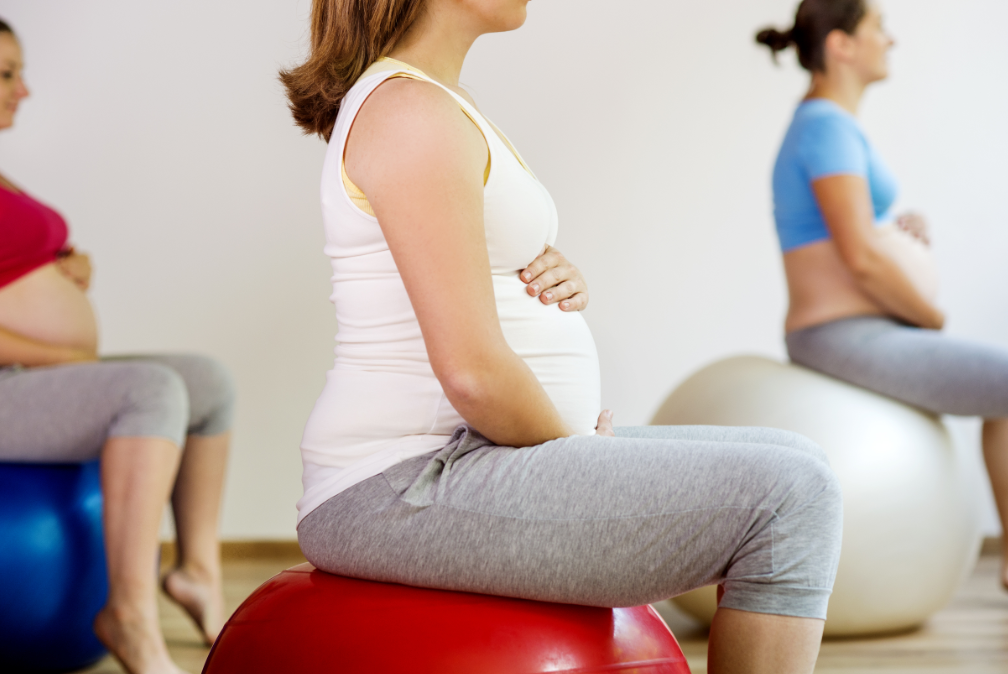 Group of pregnant women in exercise class, sitting on stability balls while holding stomach.s