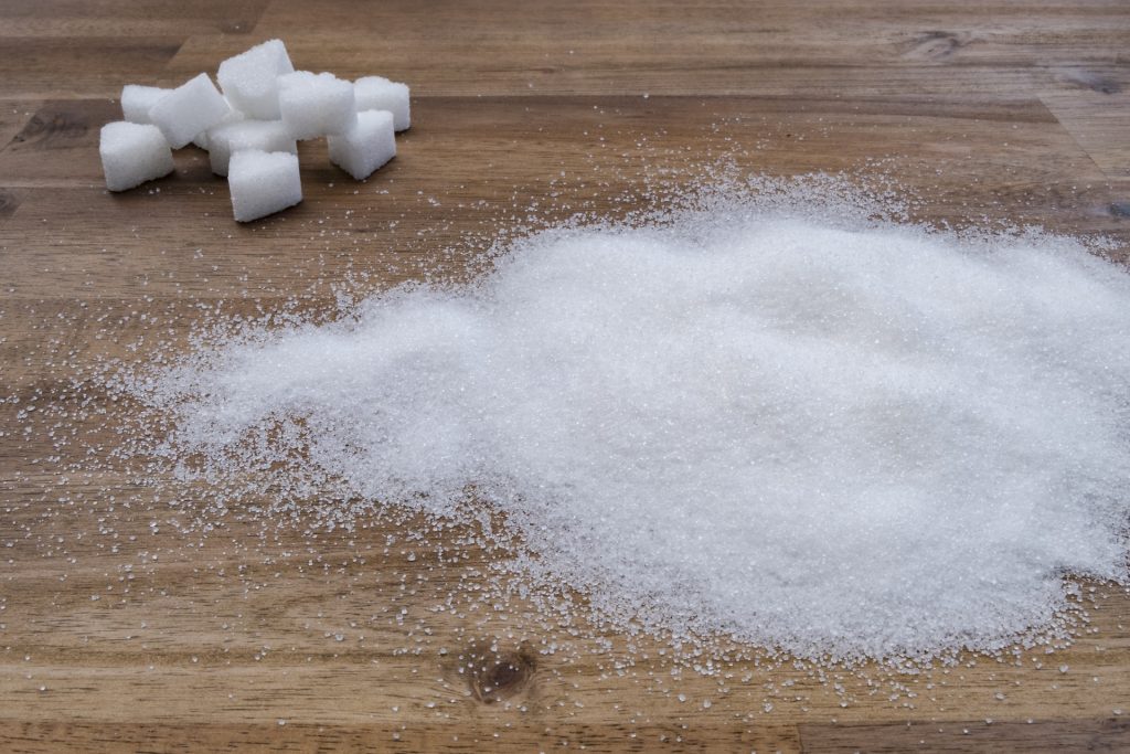 Sugar cubes and a pile of sugar on a wood surface.