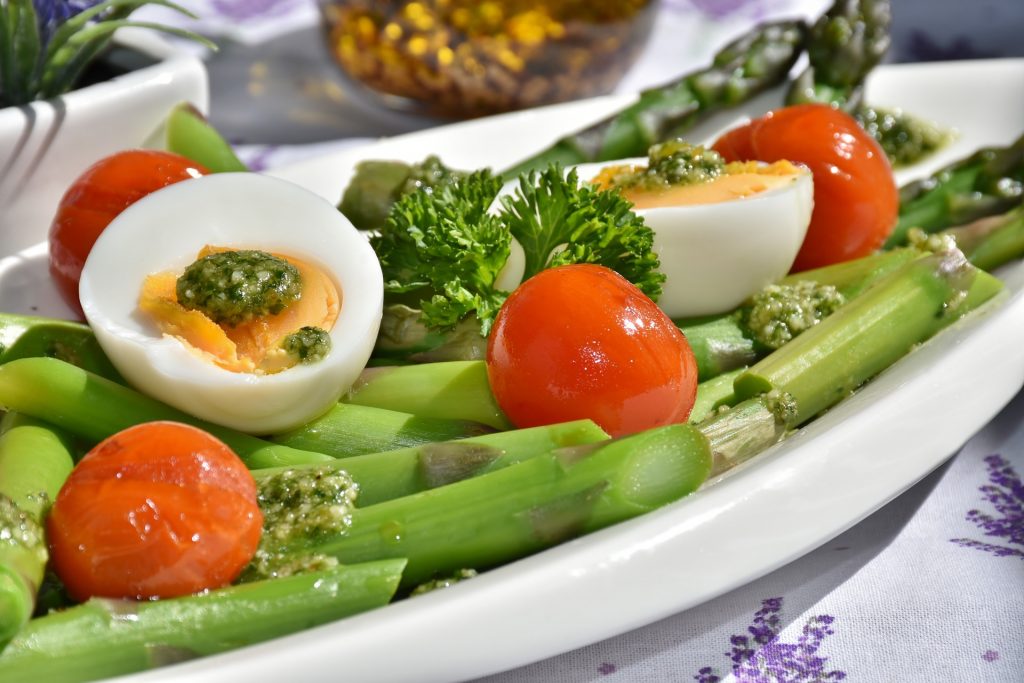 Salad with asparagus, tomatoes, eggs and pesto, garnished with herbs.