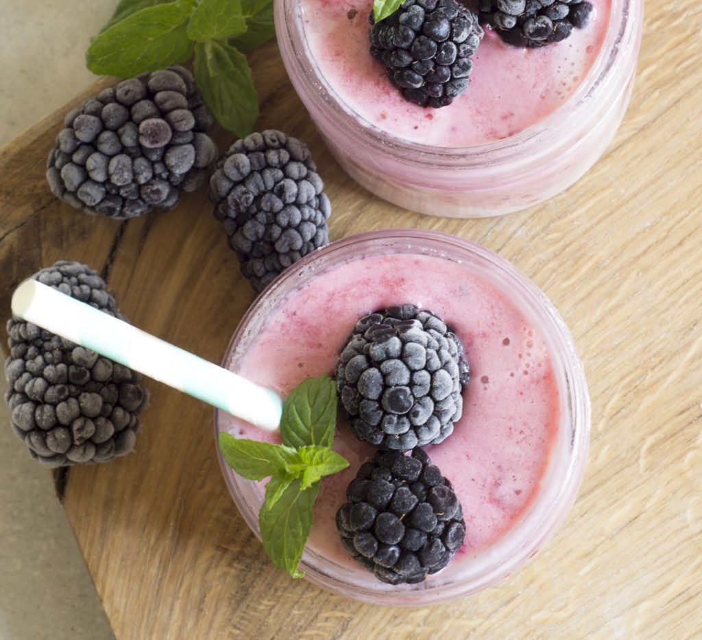 Frozen berries on top of pink smoothie, with mint and a paper straw.
