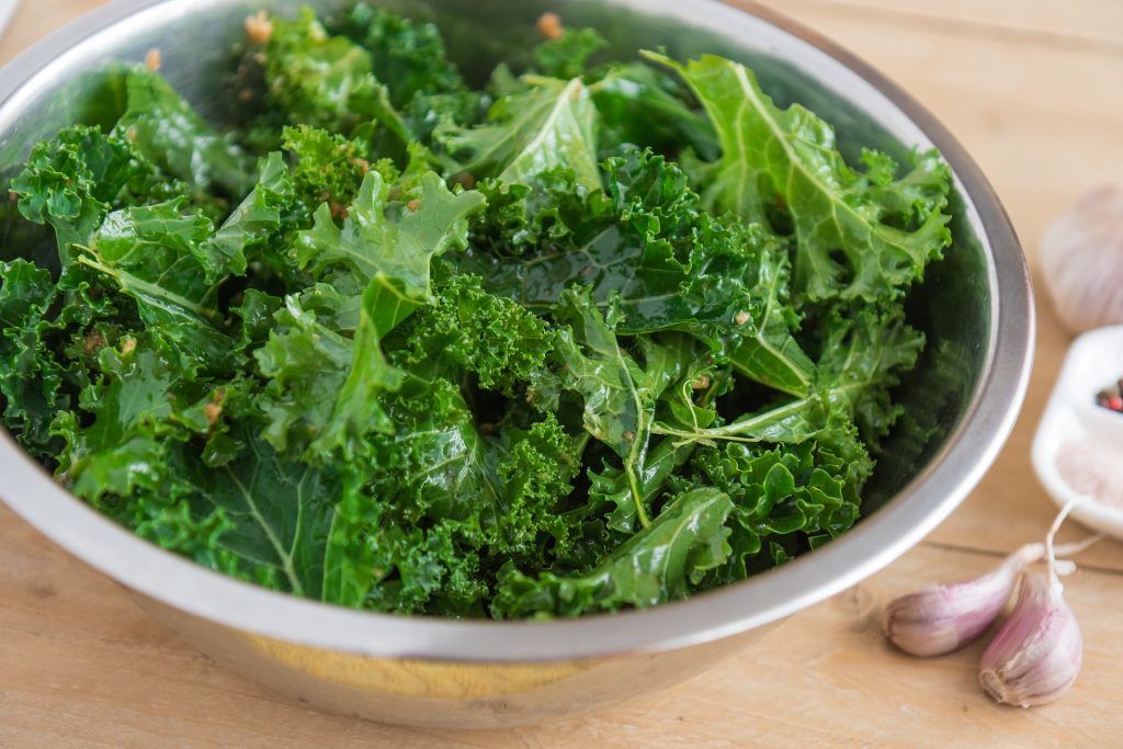 Chopped kale in bowl with dressing and seasonings.