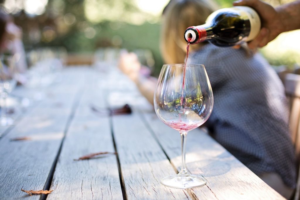 Red wine being poured into glass on outdoor table.