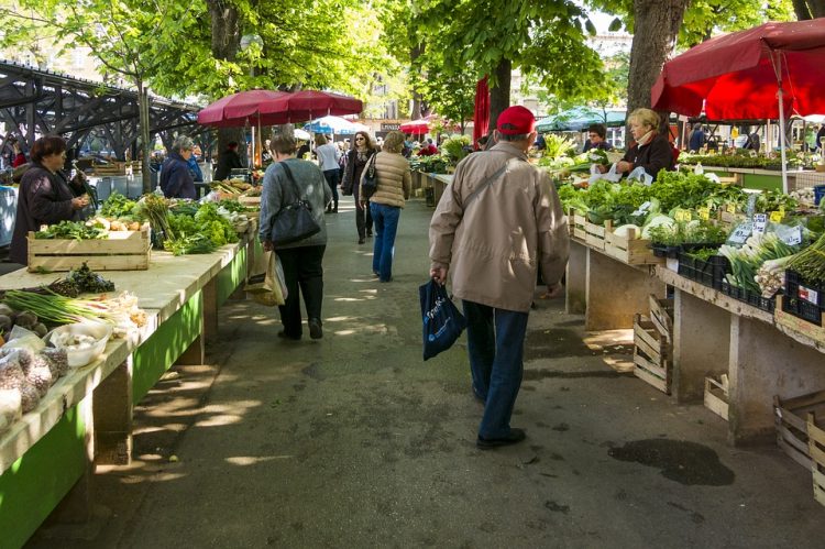 Outdoor farmer's market with customers strolling down isle of produce.