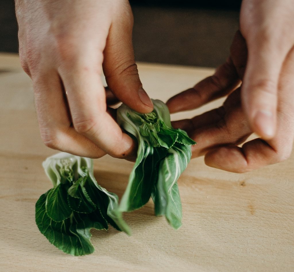 Person handling bok choy with their hands on a wooden cutting board.