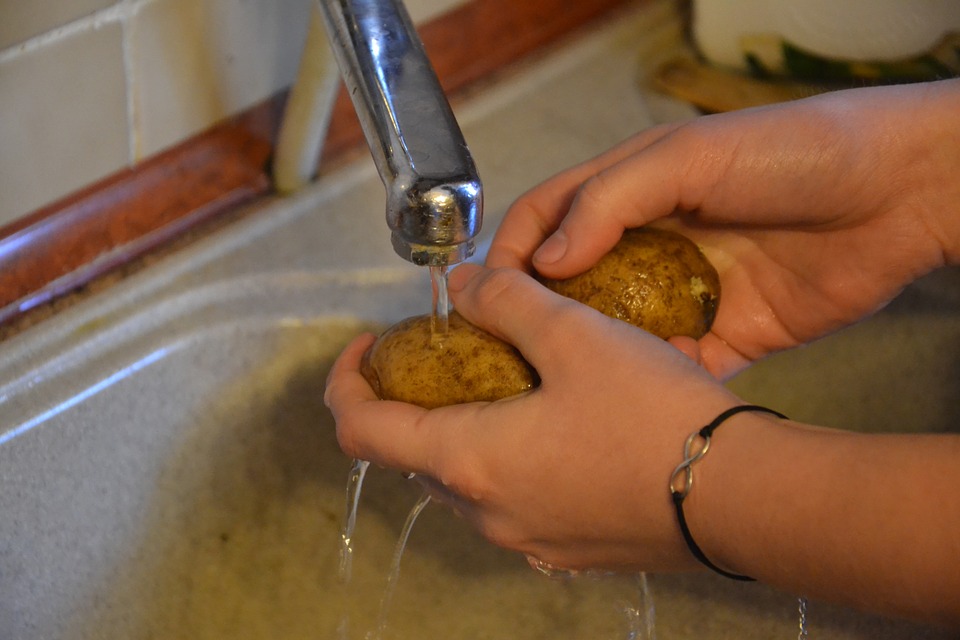 Woman washing potatoes in sink under water.