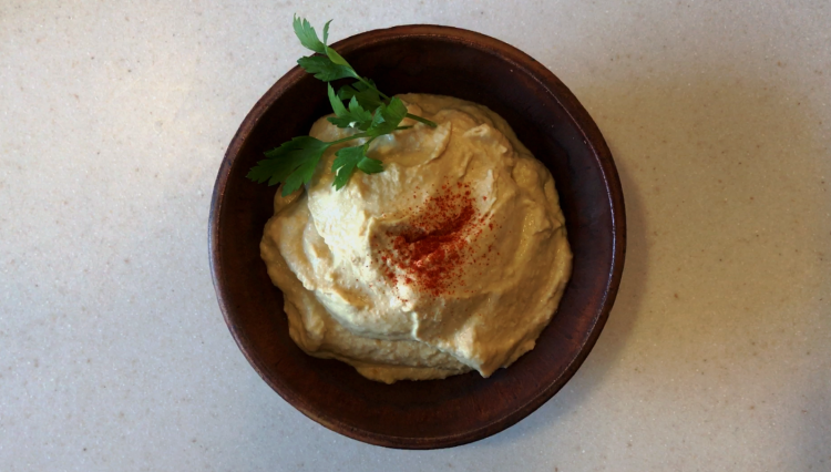 hummus in a bowl, garnished with parsley and paprika.