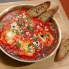 Shakshuka in a pan, paired with crispy bread and topped with feta cheese and cilantro.