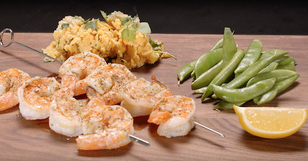 Grilled shrimp on cutting board with chickpea puree, sugar snap peas and cut lemon wedge.
