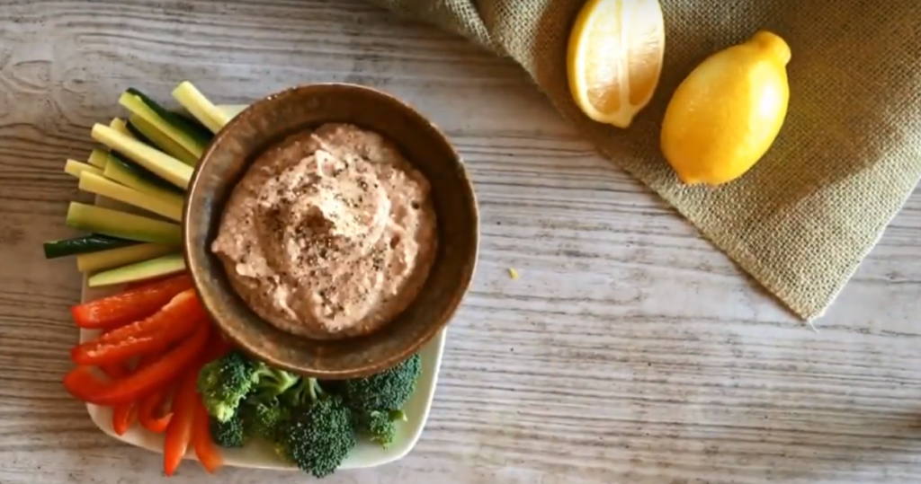 lemony white bean dip, on a plate with cut vegetables, including broccoli, red bell pepper and cucumber.
