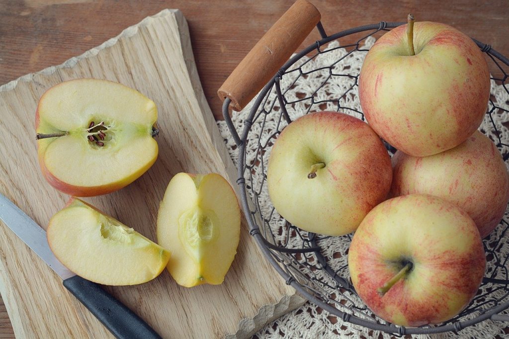 Bowl of whole apples beside small cutting board with cut apples.
