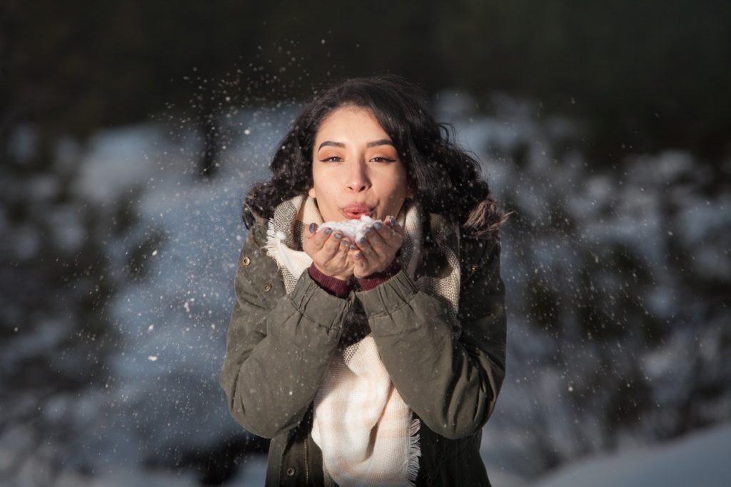 Woman holding snow in hands blowing snow at the camera.