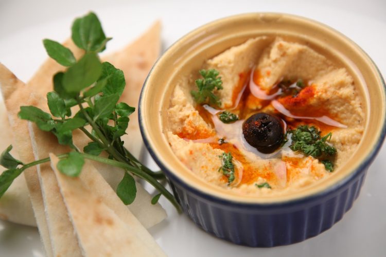 Hummus in a bowl, topped with olive oil, paprika, and an olive.