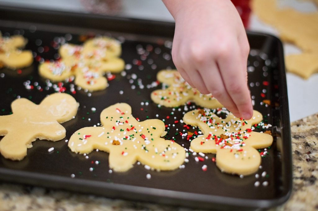 Child's hand decorating gingerbread cookie dough with red and green sprinkles.