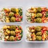 Four Tupperware boxes with rice, carrots, potatoes, falafel, chickpeas, kale and sweet peppers.