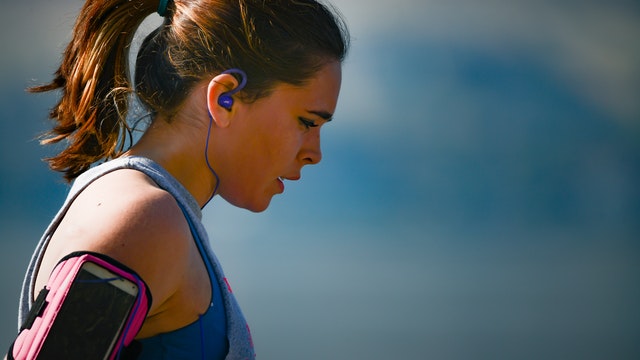 WOman wearing athletic headphones, armband with phone and running.