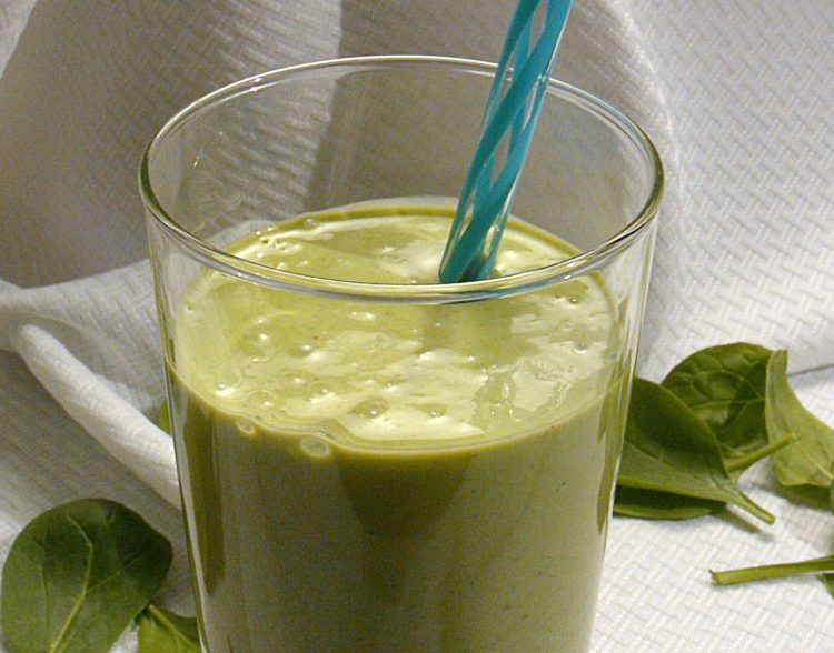 Green peanut butter smoothie in a glass with a reusable straw.
