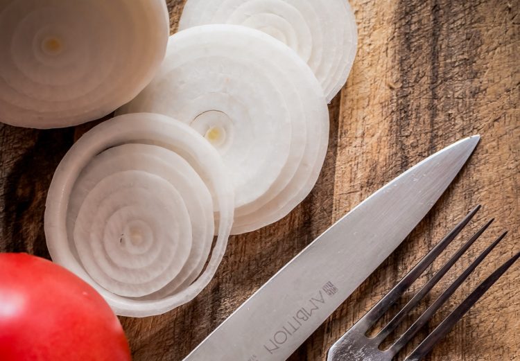 Cut onions, apple on wooden cutting board with knife and fork.