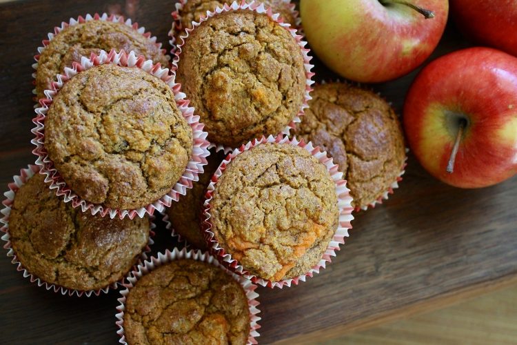 apple muffins cooling on table next to fresh apples.