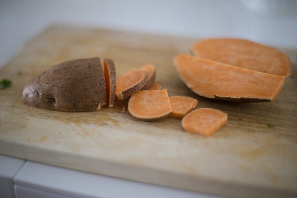 Uncooked sweet potato cut on wooden cutting board. The sweet potato has been cut into various sizes to show its orange center.